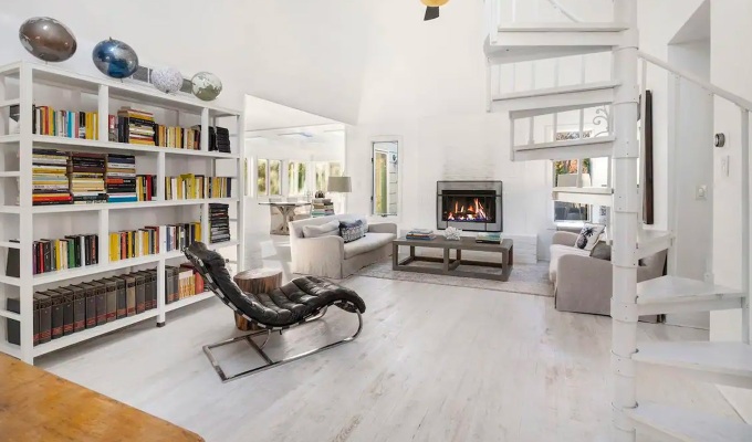Best Airbnbs in the Hamptons - A modern living room with large bookshelves lining one wall, a modern recliner chair and spiral staircase.