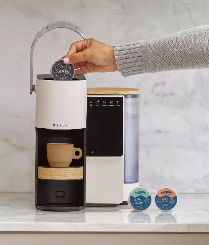 bruvi review: bruvi single-serve coffee macine on kitchen counter with a mug, and a person putting a B-Pod into the machine