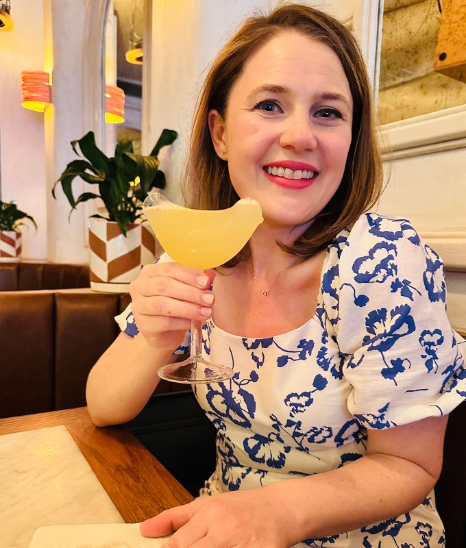 restaurant trends 2023: rachel bowie in a white and blue dress, smiling and holding a cocktail in a bird-shaped glass