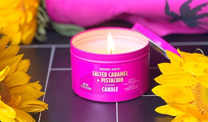 new at trader joe's june 2023: salted caramel pistachio candle in a hot pink tin on black tiles, surrounded by flowers