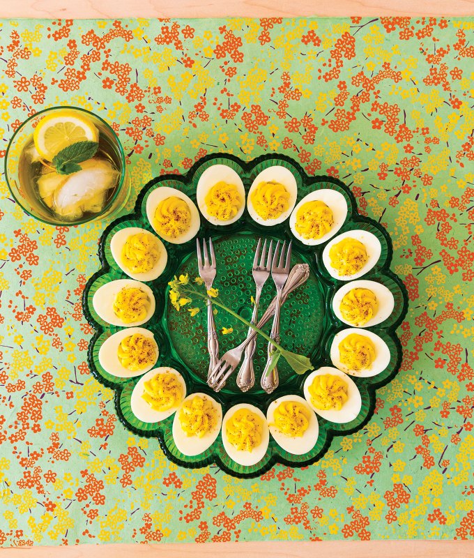 wasabi deviled eggs recipe: green platter of wasabi deviled eggs atop a floral tablecloth, next to a glass of mint-topped tea